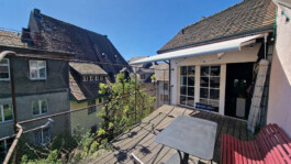 Dachterrasse mit Tisch, Stühlen, roter Bank und Blick über die Dächer der Altstadt von Laufenburg CH.