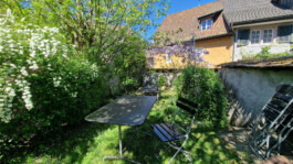 Privater Gartensitzplatz mit Tisch, Stühlen, blühenden Sträuchern und Altstadthäusern in Laufenburg CH.