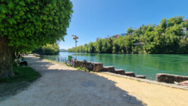 Rheinpromenade in Laufenburg CH mit Sitzbänken, Fahrrädern und Blick auf den grünen Rhein.